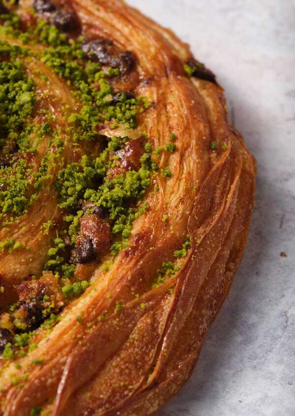 Close-up of a flaky, golden pastry topped with vibrant green pistachio crumbs, showcasing its layered texture and sugary glaze.